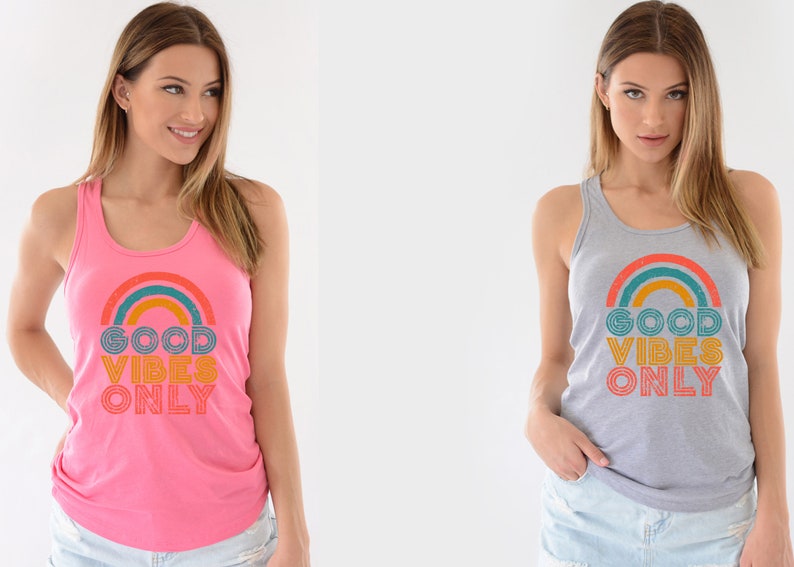 May include: Two women wearing tank tops with a rainbow and the text "Good Vibes Only" printed on the front. The tank top on the left is pink and the tank top on the right is gray.