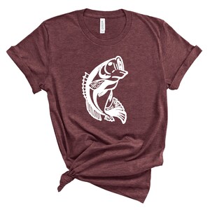 以下が含まれることがあります： 水から飛び出す魚の白いシルエットが描かれた、マルーンのTシャツです。