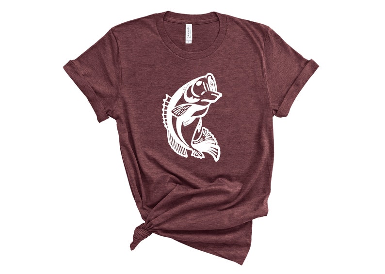 以下が含まれることがあります： 水から飛び出す魚の白いシルエットが描かれた、マルーンのTシャツです。