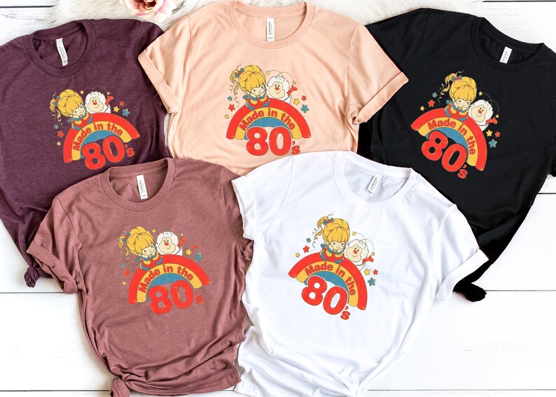 Puede incluir: Cinco camisetas de diferentes colores con un gr&aacute;fico de dibujos animados retro de dos figuras en un arco&iacute;ris con el texto "Made in the 80's".