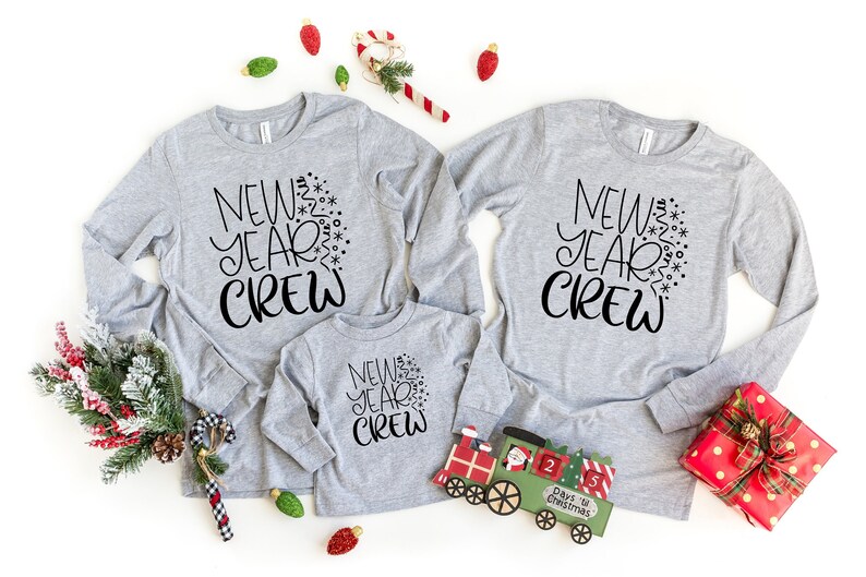Three long sleeved grey shirts with black text on them surrounded by Christmas decorations