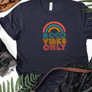 May include: A navy blue t-shirt with a rainbow graphic and the text "GOOD VIBES ONLY" in a vintage style font.