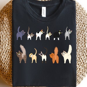 May include: A black t-shirt with a graphic of ten cats with their tails up in the air. The cats are all different colors and breeds.