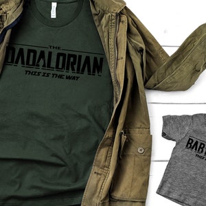 May include: Two t-shirts with a Star Wars themed design. The larger shirt is dark green with the text "The Dadalorian - This is the Way". The smaller shirt is grey with the text "The BabyLorian - This is the Way".