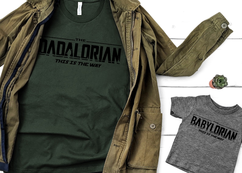 May include: Two t-shirts with a Star Wars themed design. The larger shirt is dark green with the text "The Dadalorian - This is the Way". The smaller shirt is grey with the text "The BabyLorian - This is the Way".