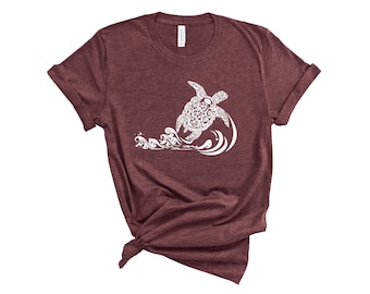 May include: A maroon t-shirt featuring a white graphic of a turtle swimming in a wave. The turtle and wave are made up of intricate patterns.