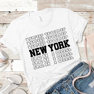 May include: White t-shirt with a black graphic print of the word "NEW YORK" repeated in a stacked pattern.