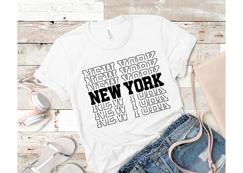May include: White t-shirt with a black graphic print of the word "NEW YORK" repeated in a stacked pattern.