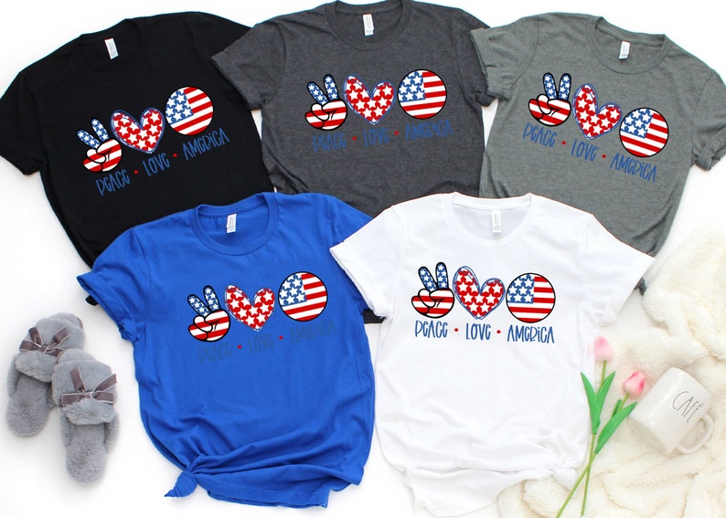 May include: Four t-shirts with a peace sign, heart, and American flag design. The shirts are in black, gray, blue, and white.