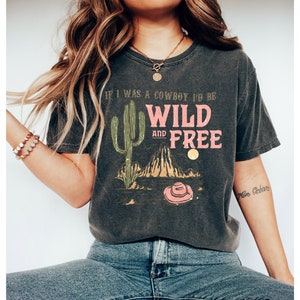 May include: A dark gray t-shirt with a graphic print of a cactus, mountains, and a cowboy hat. The text on the shirt reads "If I was a cowboy I'd be wild and free".