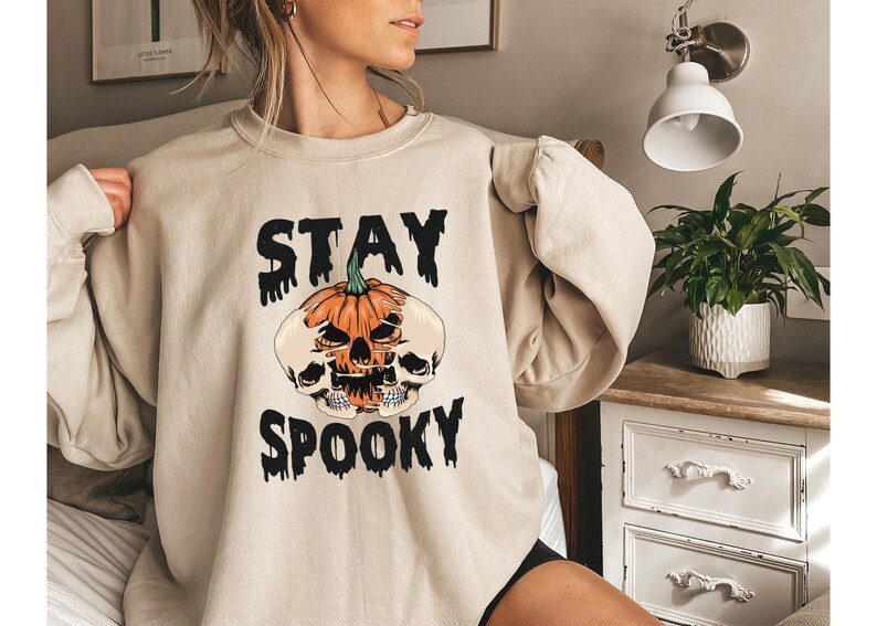 以下が含まれることがあります： ハロウィーンをテーマにしたベージュのスウェットシャツ。デザインは、スカルと黒い文字「STAY SPOOKY」が付いたジャック・オー・ランタンが特徴です。スウェットシャツは長袖で、ゆったりとしたフィット感です。