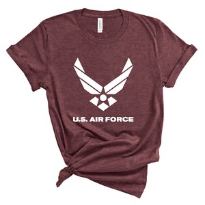 May include: A maroon t-shirt with a white U.S. Air Force logo and the words "U.S. Air Force" printed on the front.
