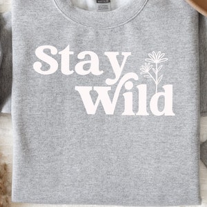 May include: Gray sweatshirt with white text that reads "Stay Wild" and a stylized flower graphic.
