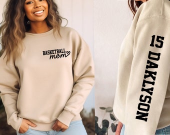 May include: Beige sweatshirt with the text "Basketball Mom" and a heart on the front. The left sleeve has the text "15 DAKLYSON" printed vertically.
