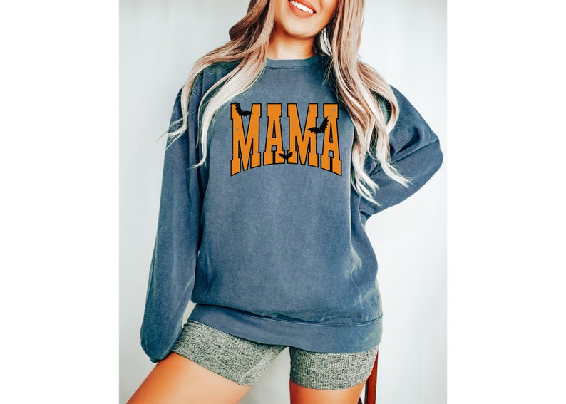 May include: A blue-grey sweatshirt with the word "MAMA" in orange block letters. The word "MAMA" has a bat on top of each letter "A". The sweatshirt is a crew neck style.