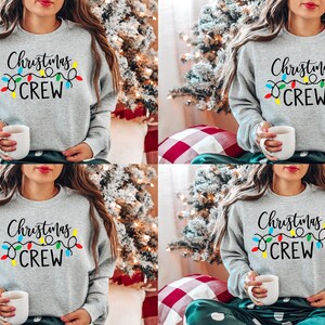 May include: Four women wearing gray sweatshirts with the text "Christmas Crew" and colorful string lights. The sweatshirts are a casual, comfortable style.