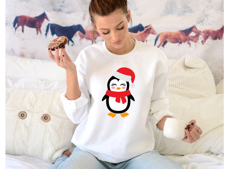 May include: White sweatshirt with a cartoon penguin wearing a red Santa hat and scarf. The penguin is smiling and has black eyes.