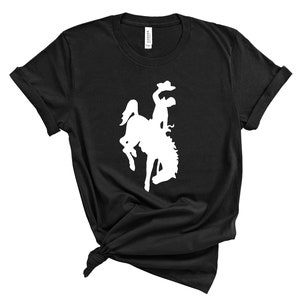 May include: A black t-shirt with a white silhouette of a cowboy riding a bucking horse.