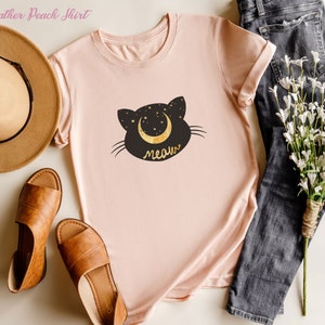 May include: A heather peach t-shirt with a black cat silhouette and a crescent moon with stars. The text "meow" is written below the cat.