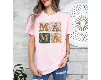 May include: Pink t-shirt with a floral print design that spells out "MAMA" in gold letters.