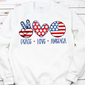 May include: White sweatshirt with a peace sign, heart, and American flag design. The text "Peace Love America" is printed below the design.