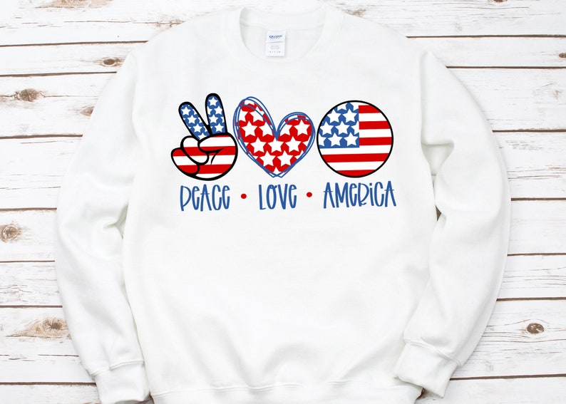 May include: White sweatshirt with a peace sign, heart, and American flag design. The text "Peace Love America" is printed below the design.