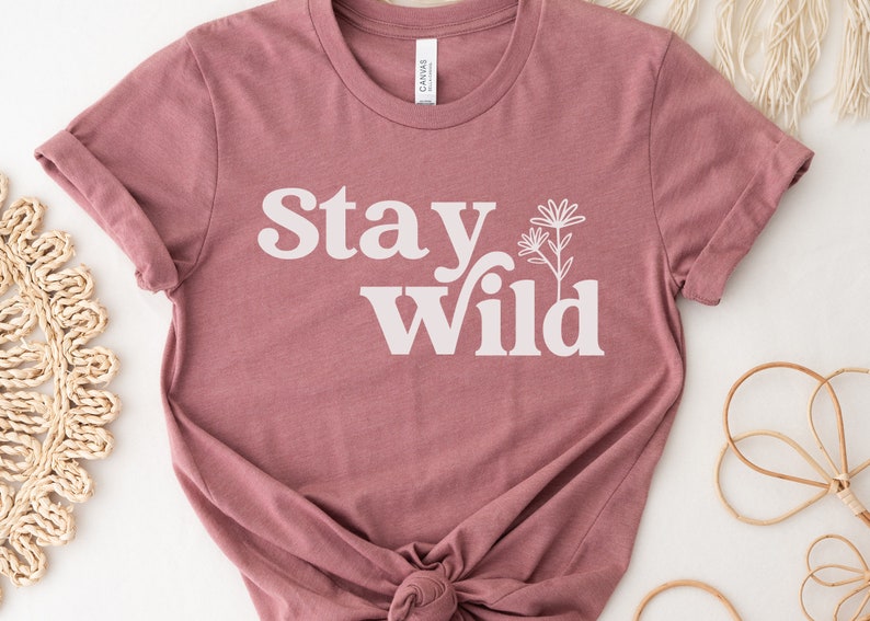 May include: A mauve t-shirt with the text "Stay Wild" in white lettering with a stylized flower graphic.