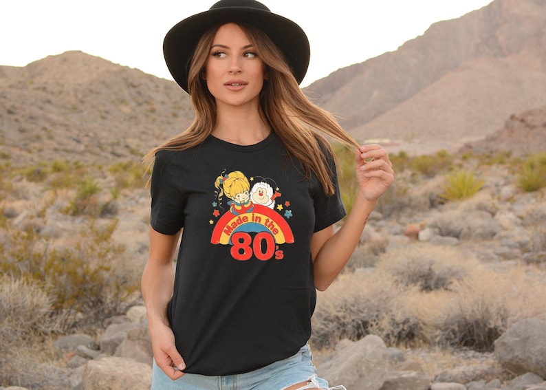 Puede incluir: Camiseta negra con un gr&aacute;fico de arco&iacute;ris y estrellas. El gr&aacute;fico presenta dos personajes de dibujos animados y el texto "Made in the 80's".