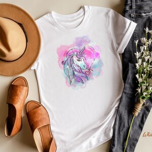 May include: White t-shirt with a watercolor design of a unicorn inside a heart. The unicorn is purple and white with a pink and blue background.