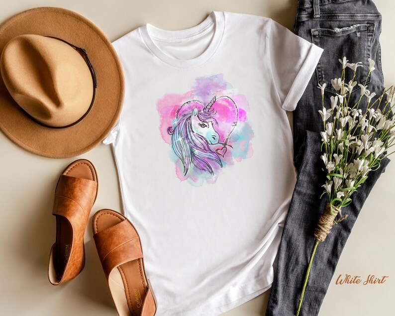 May include: White t-shirt with a watercolor design of a unicorn inside a heart. The unicorn is purple and white with a pink and blue background.