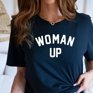 May include: A black t-shirt with the text "WOMAN UP" printed in white on the front.