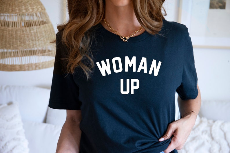 May include: A black t-shirt with the text "WOMAN UP" printed in white on the front.