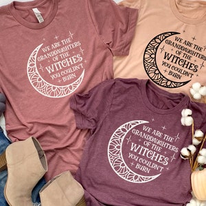 May include: Three t-shirts with a moon and stars design and the text "We are the granddaughters of the witches you couldn't burn". The shirts are in different colors: maroon, peach, and burgundy.