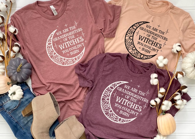 May include: Three t-shirts with a moon and stars design and the text "We are the granddaughters of the witches you couldn't burn". The shirts are in different colors: maroon, peach, and burgundy.