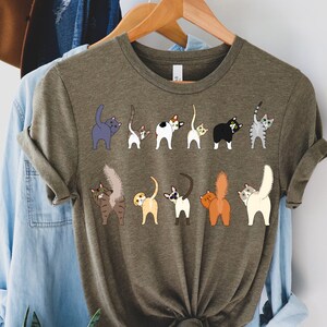 May include: A green t-shirt with a graphic of multiple cats with their tails up in the air. The cats are all different colors and breeds.