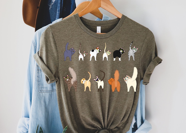 May include: A green t-shirt with a graphic of multiple cats with their tails up in the air. The cats are all different colors and breeds.
