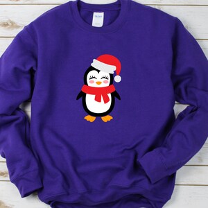 May include: Purple long-sleeved sweatshirt with a cartoon penguin wearing a red Santa hat and a red scarf.