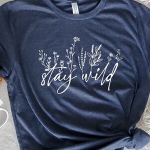 May include: A navy blue t-shirt with a white floral design and the text "stay wild" printed on the front.