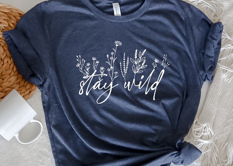 May include: A navy blue t-shirt with a white floral design and the text "stay wild" printed on the front.
