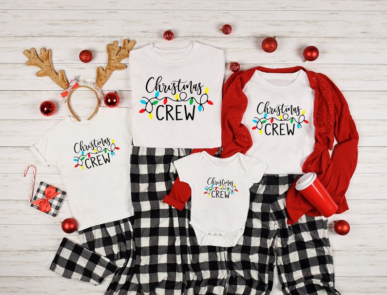 May include: A family of four wearing matching white pajamas with black and white plaid pants. The shirts have the text "Christmas Crew" with a string of colorful lights.