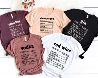May include: Five t-shirts with different alcohol names and nutrition facts printed on them. The shirts are in various colors, including maroon, peach, black, brown, and white.