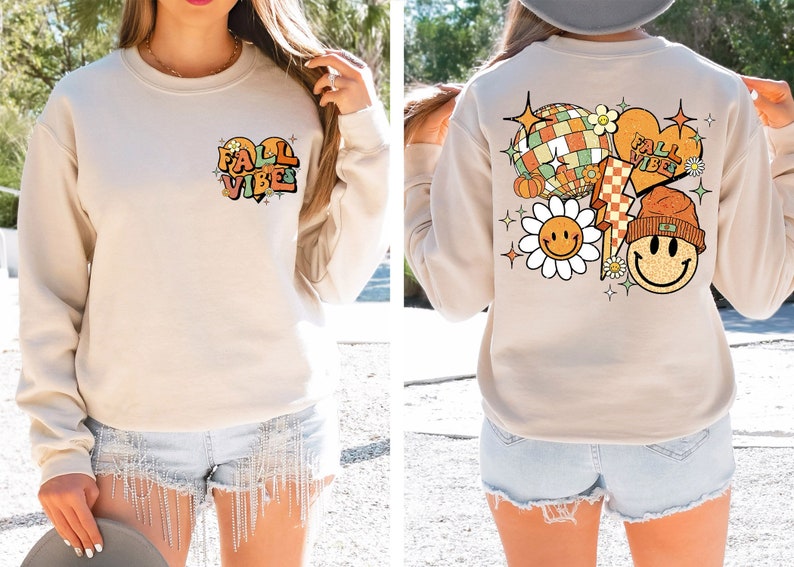 May include: A beige sweatshirt with a graphic print of a heart with the text "Fall Vibes" on the front and a graphic print of a smiley face, a heart with the text "Fall Vibes", a lightning bolt, a pumpkin, a disco ball, and a flower on the back.