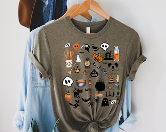 Può includere: T-shirt verde oliva con una collezione di illustrazioni a tema Halloween. Il design include zucche, fantasmi, pipistrelli, teschi e un personaggio ispirato a Mickey Mouse. È visibile anche la parola "BOO".
