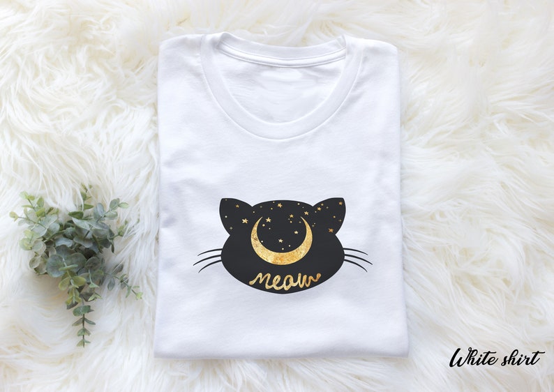 May include: White t-shirt with a black cat silhouette design. The cat has a crescent moon with stars on its head and the word "meow" underneath.