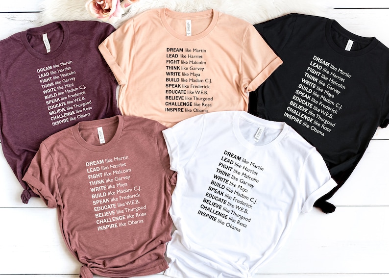 May include: Five t-shirts in different colors with the text "DREAM like Martin, LEAD like Harriet, FIGHT like Malcolm, THINK like Garvey, WRITE like Maya, BUILD like Madam CJ, SPEAK like Frederick, EDUCATE like WEB, BELIEVE like Thurgood, CHALLENGE like Rosa, INSPIRE like Obama" printed on them.