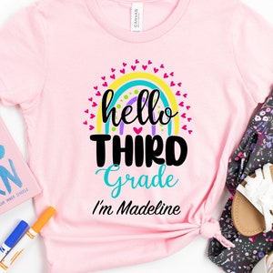 May include: Pink t-shirt with a rainbow and the text "hello third grade I'm Madeline"
