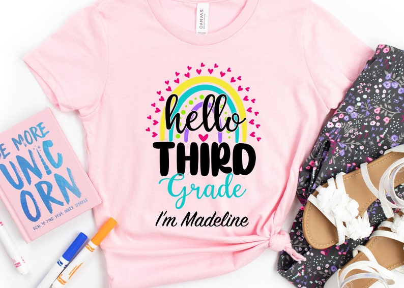 May include: Pink t-shirt with a rainbow and the text "hello third grade I'm Madeline"