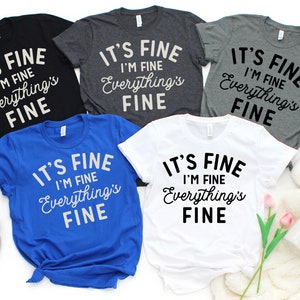 May include: Five t-shirts in different colors with the same text printed on them: "It's Fine I'm Fine Everything's Fine".