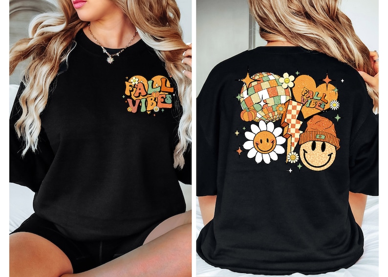 May include: Black oversized t-shirt with a graphic print of a heart with the text "Fall Vibes" on the front and a graphic print of a disco ball, pumpkin, lightning bolt, and two smiley faces with flowers on the back.