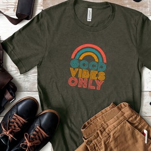 May include: A green t-shirt with a rainbow graphic and the text "GOOD VIBES ONLY" in a retro font.